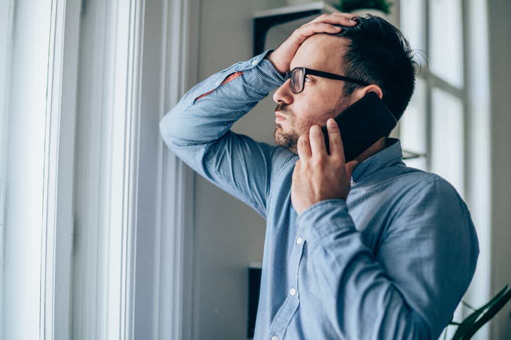 Man holds his head as he's stressed while talking on the phone